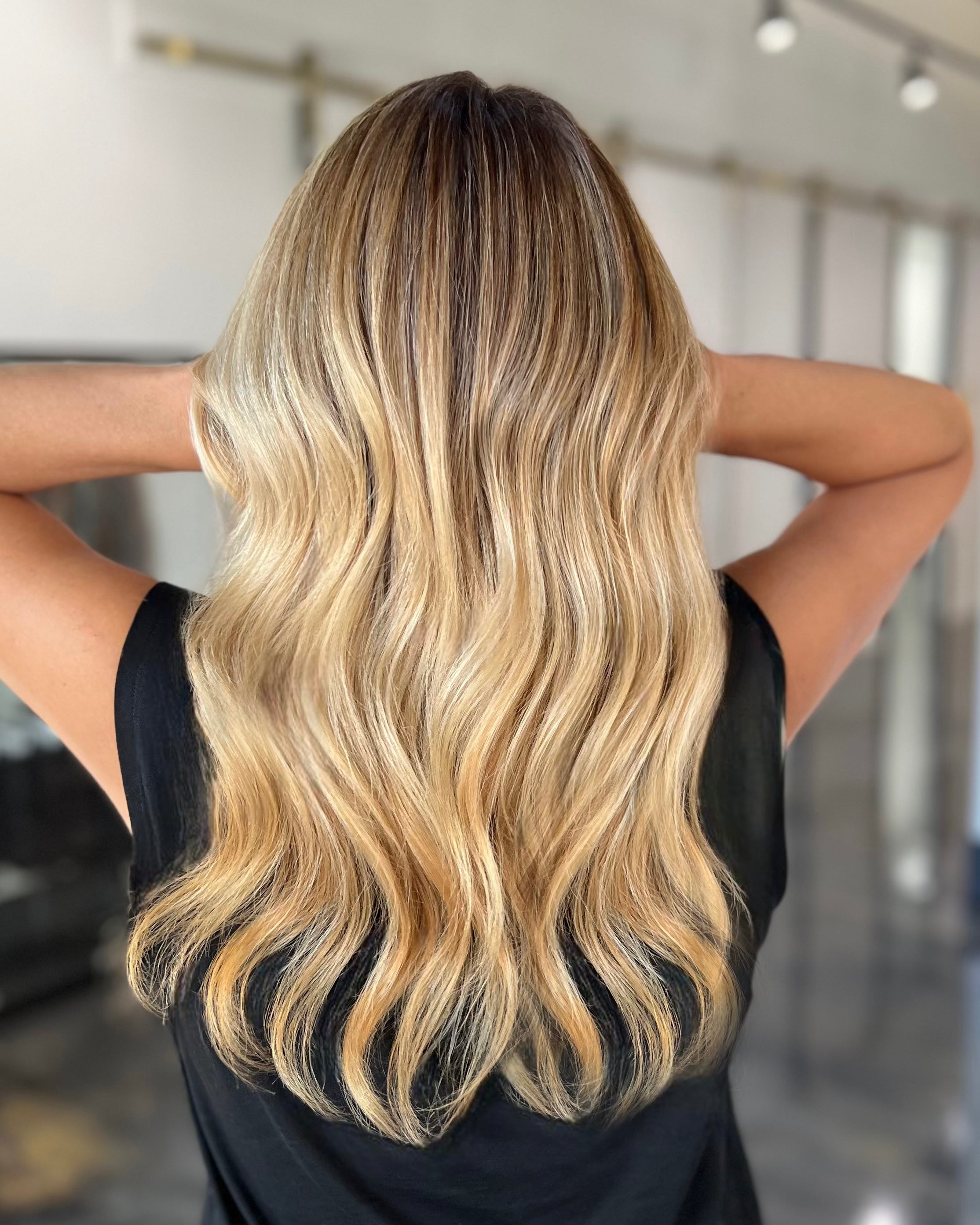 Person with long, wavy, blonde hair in a blurred indoor setting