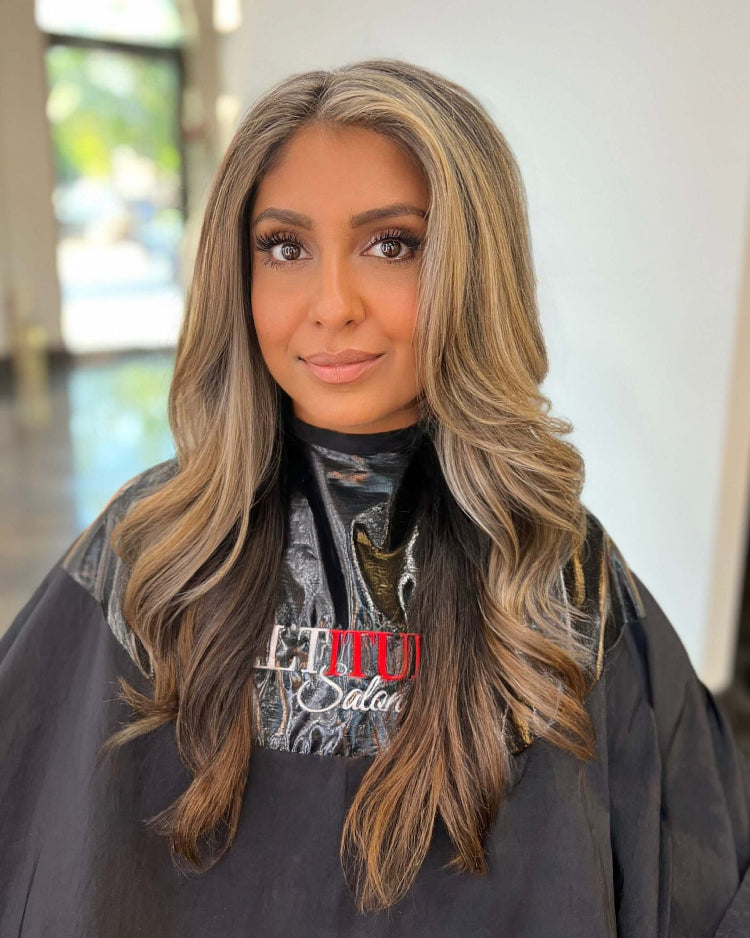 Woman with long, wavy hair wearing a salon cape indoors.